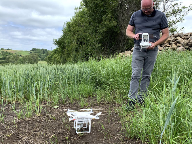 Mand med dronestyring på en grøn mark, hvor dronen står på jorden klar til flyvning