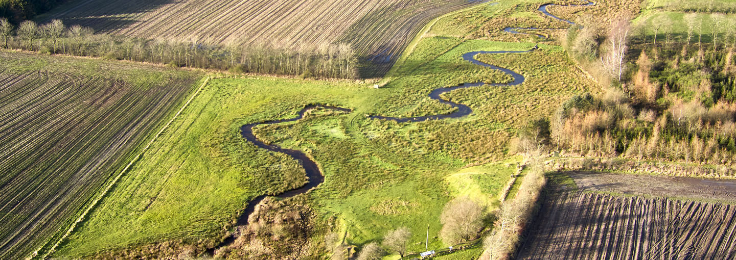 Luftfoto af landbrugsjorde med vandløb og bevoksning