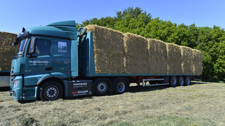 Blå lastbil med anhænger læsset med store halmballer