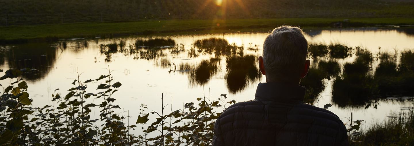 Mand står i solnedgang foran en marksø og kigger ud over landskabet