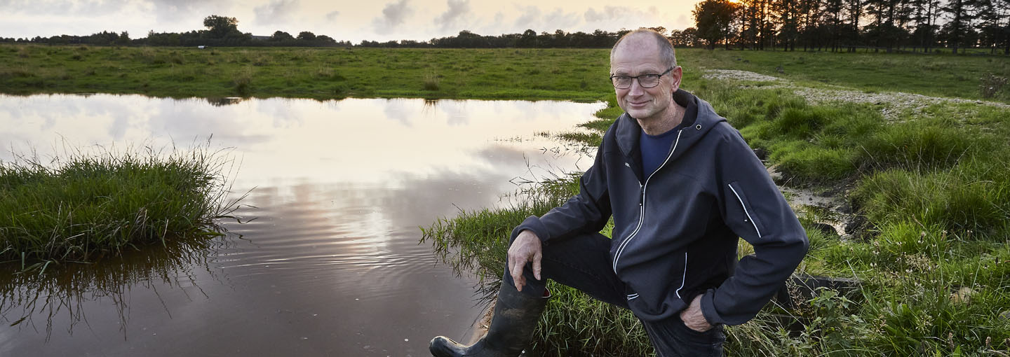 Mand stående ved opdæmning af vand på en grøn mark