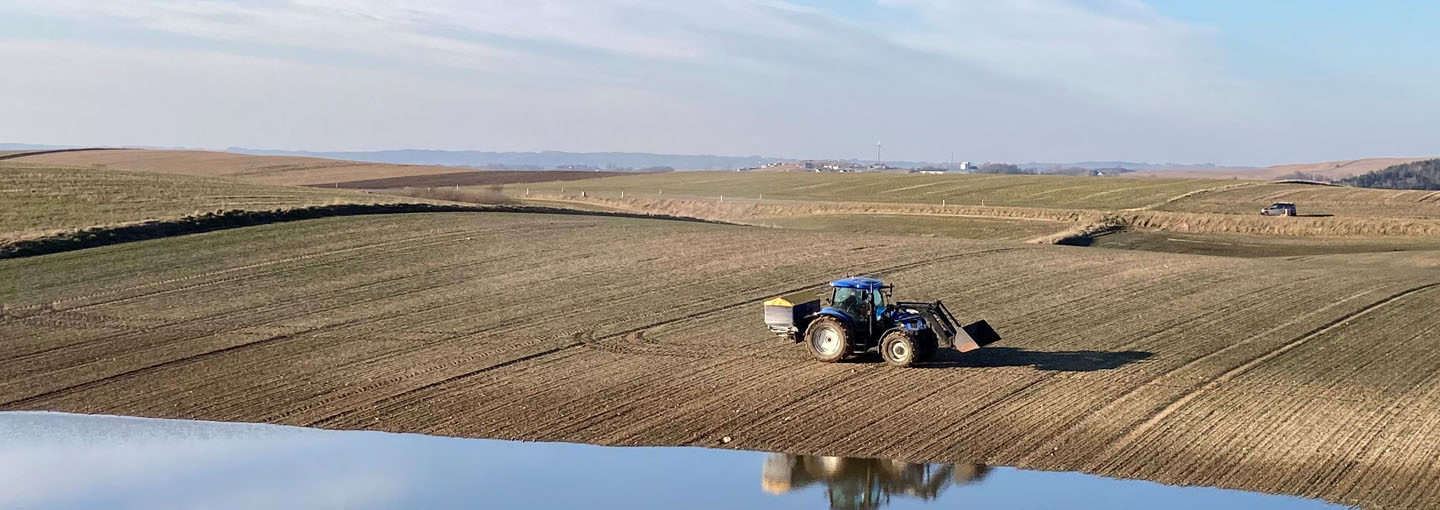 Blå traktor kører på forårsmark med frontlæsser og gødsker