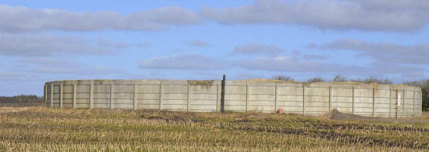 Stor rund gyllebeholder på stubbet majsmark med blå himmel og lette skyer