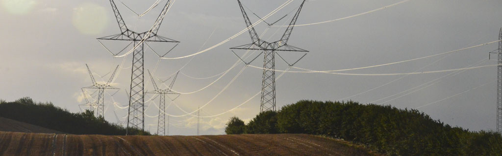 Store højspændingsmaster og elmaster på mark i naturen